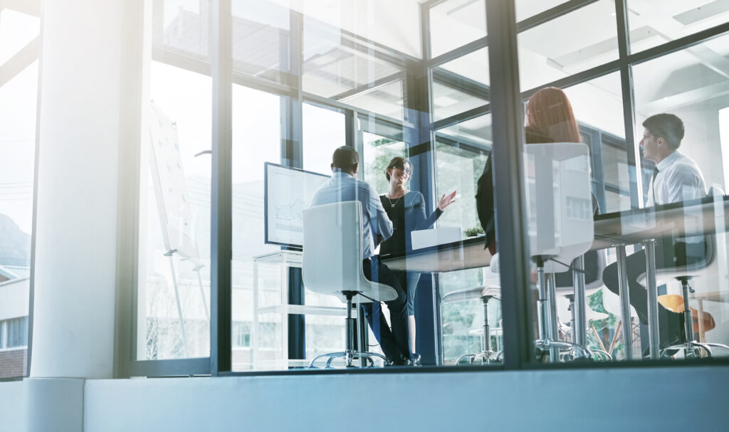 A conference room with business people in it seen through the outside window.