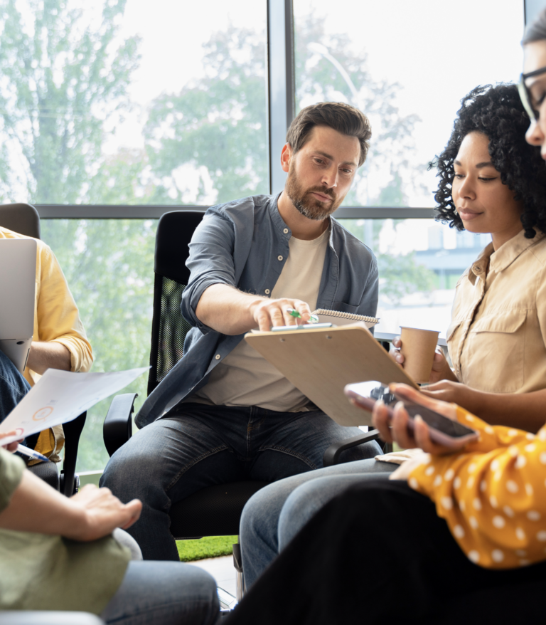 a group of people sitting in a circle pointing to a tablet.