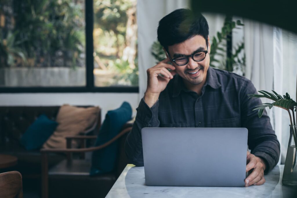 A man sitting at a desk and smiling as he looks at his laptop
