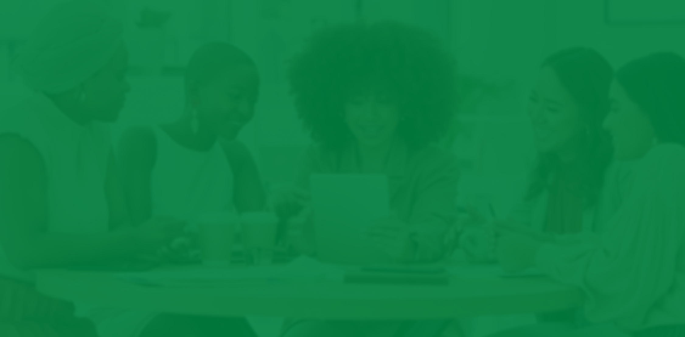 Women in business casual clothes sitting around a table looking at a tablet.