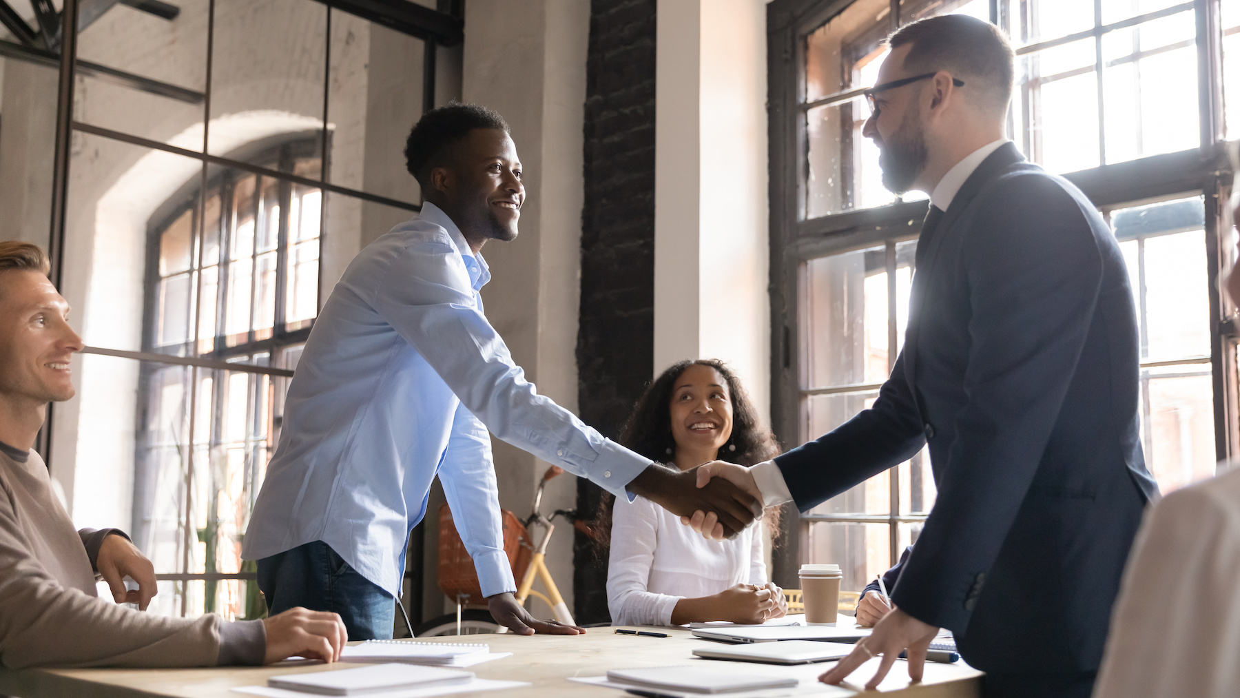 Two people shaking hands across a conference table.